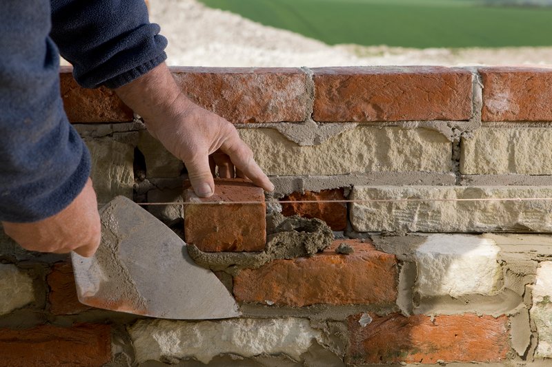 Maçon intervenant à la truelle sur un mur de briques anciennes lors d'une rénovation de façade à Bruxelles