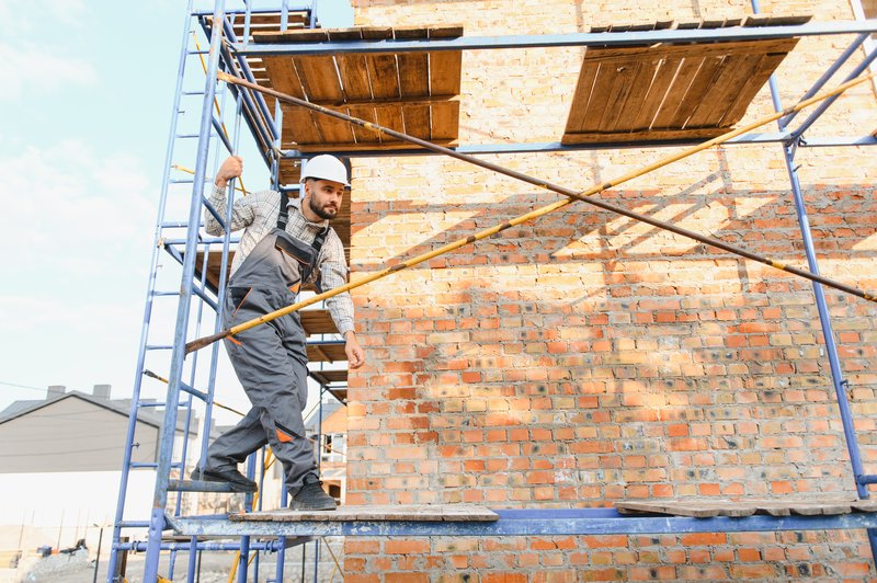 Ouvrier sur un échafaudage devant une façade en briques lors d'un chantier de ravalement