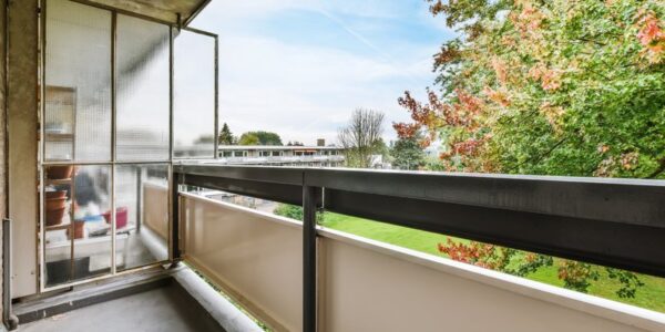 Balcon en béton d'un immeuble donnant sur un espace vert, exposé aux intempéries