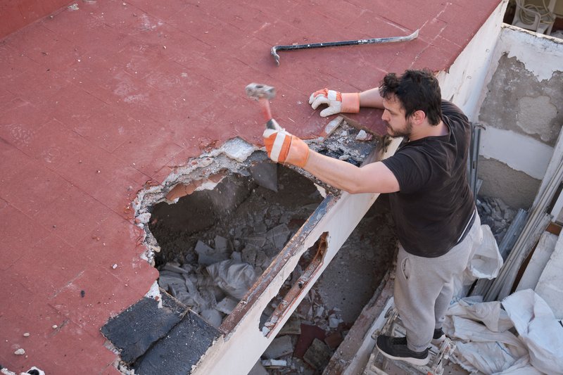Ouvrier purgeant au marteau le béton dégradé d'une dalle de balcon avant réparation