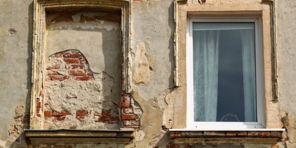 Façade ancienne dont le cimentage s’écaille autour des fenêtres et laisse voir la brique
