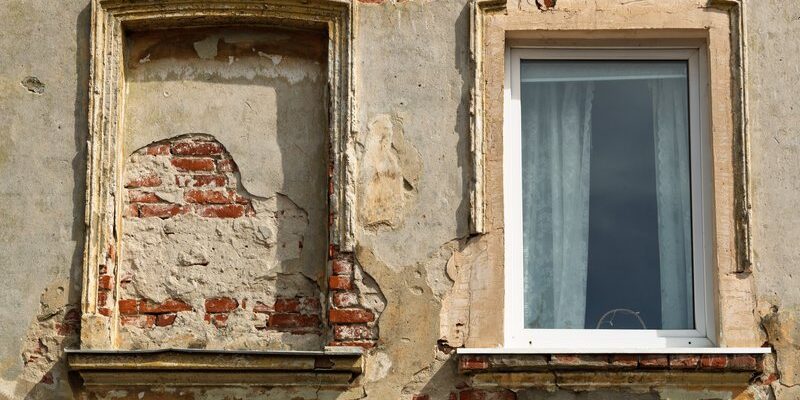 Façade ancienne dont le cimentage s’écaille autour des fenêtres et laisse voir la brique