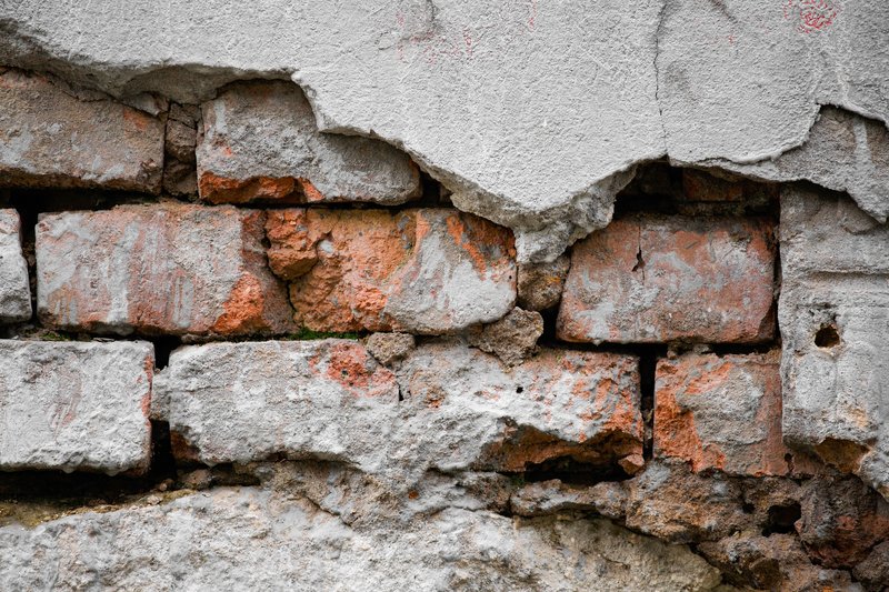 Plaque d’enduit fissurée et décollée au-dessus d’un mur en briques